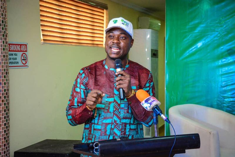 A speaker in a cap at the podium, holding a branded microphone.